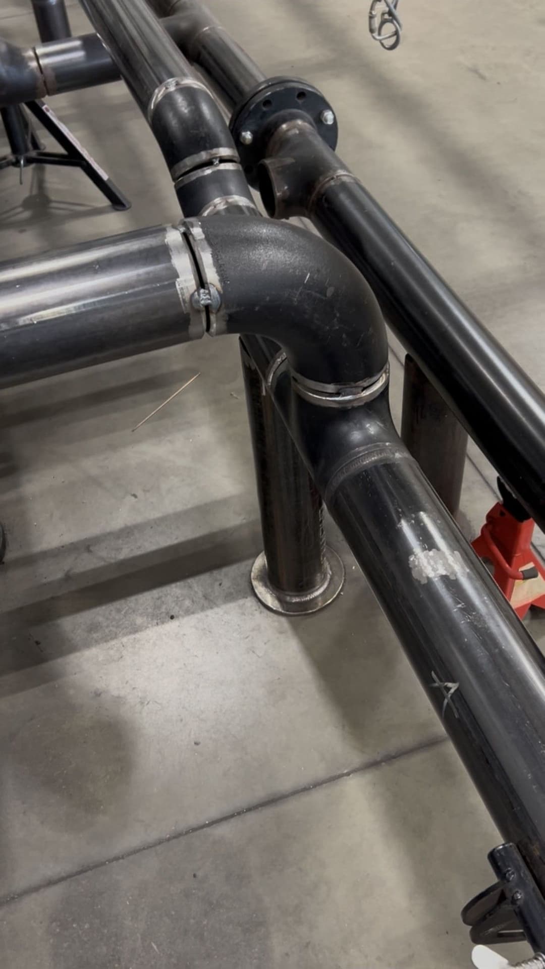 Industrial metal piping with elbows and connectors on a concrete floor.