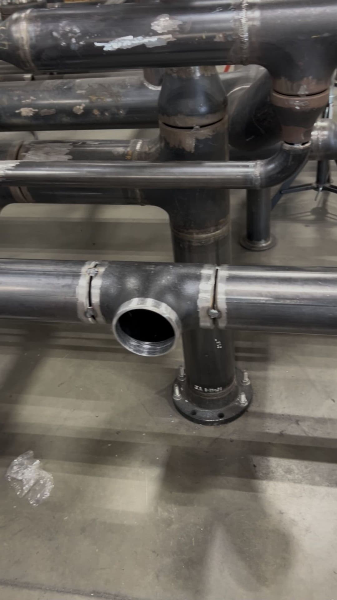 Black industrial pipes with a T-junction and welds in a factory setting.